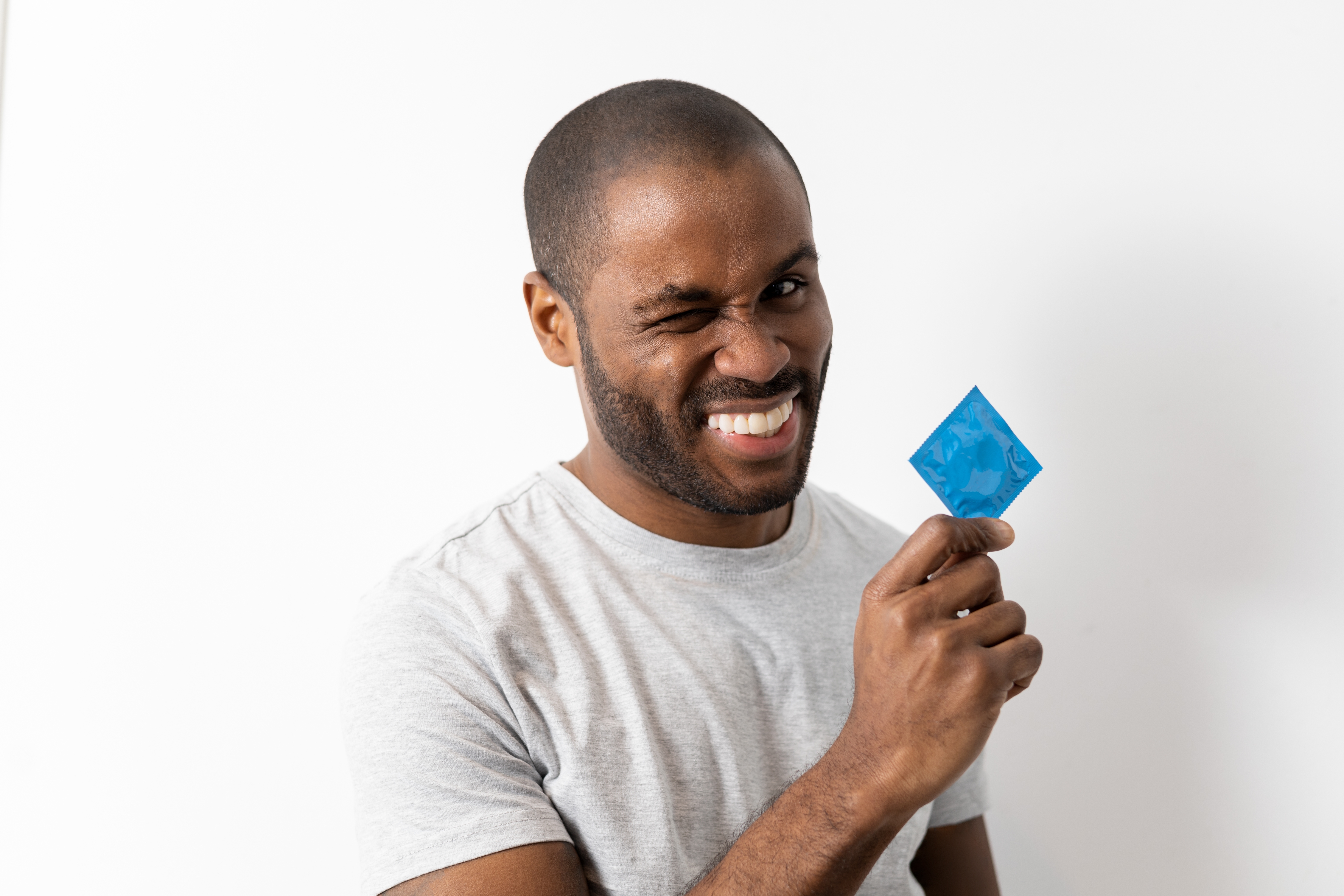 A,Curious,Dark-skinned,Man,Holds,A,Condom,While,Squinting,His