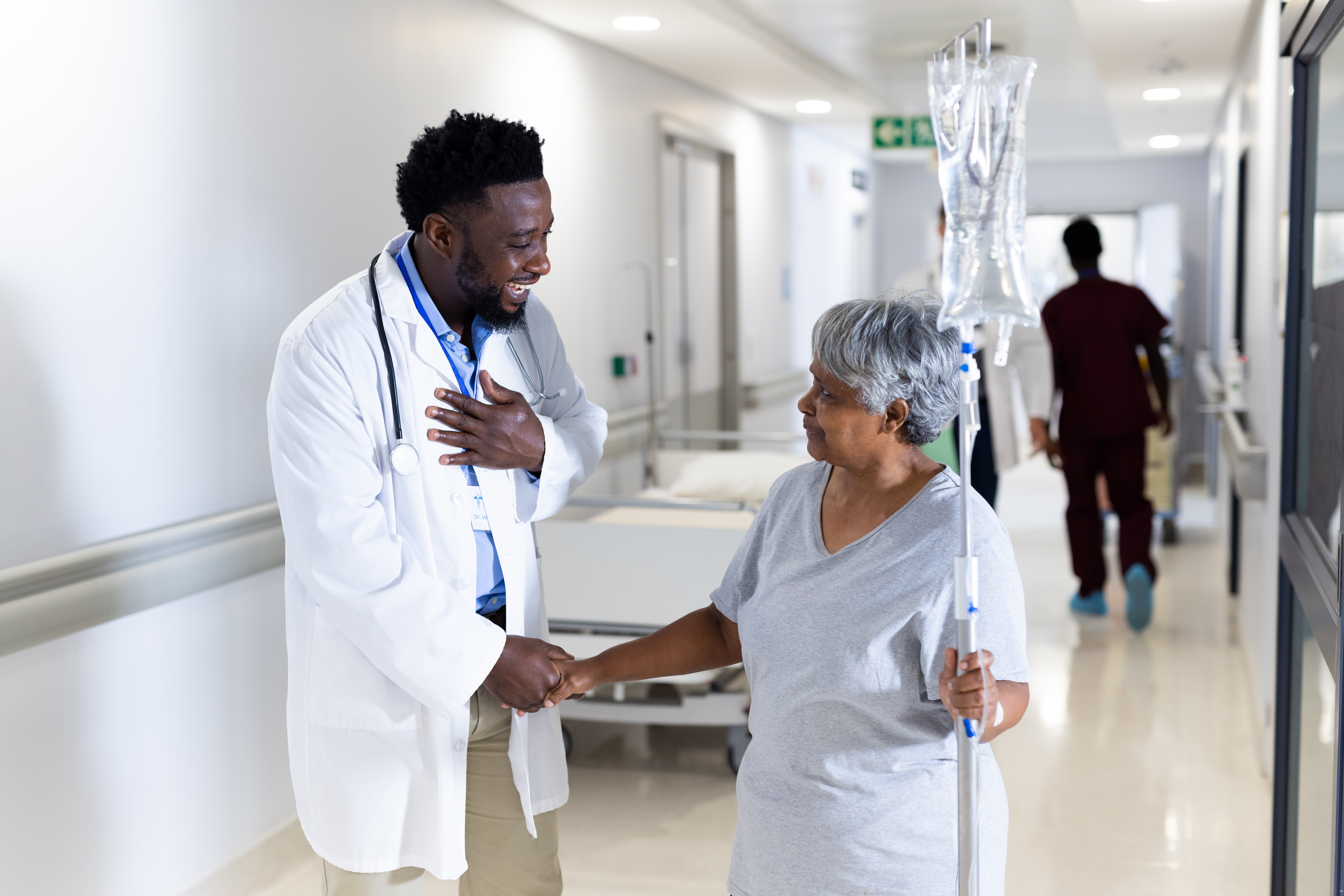 Biracial,Senior,Female,Patient,With,Drip,Shaking,Hand,Of,Happy