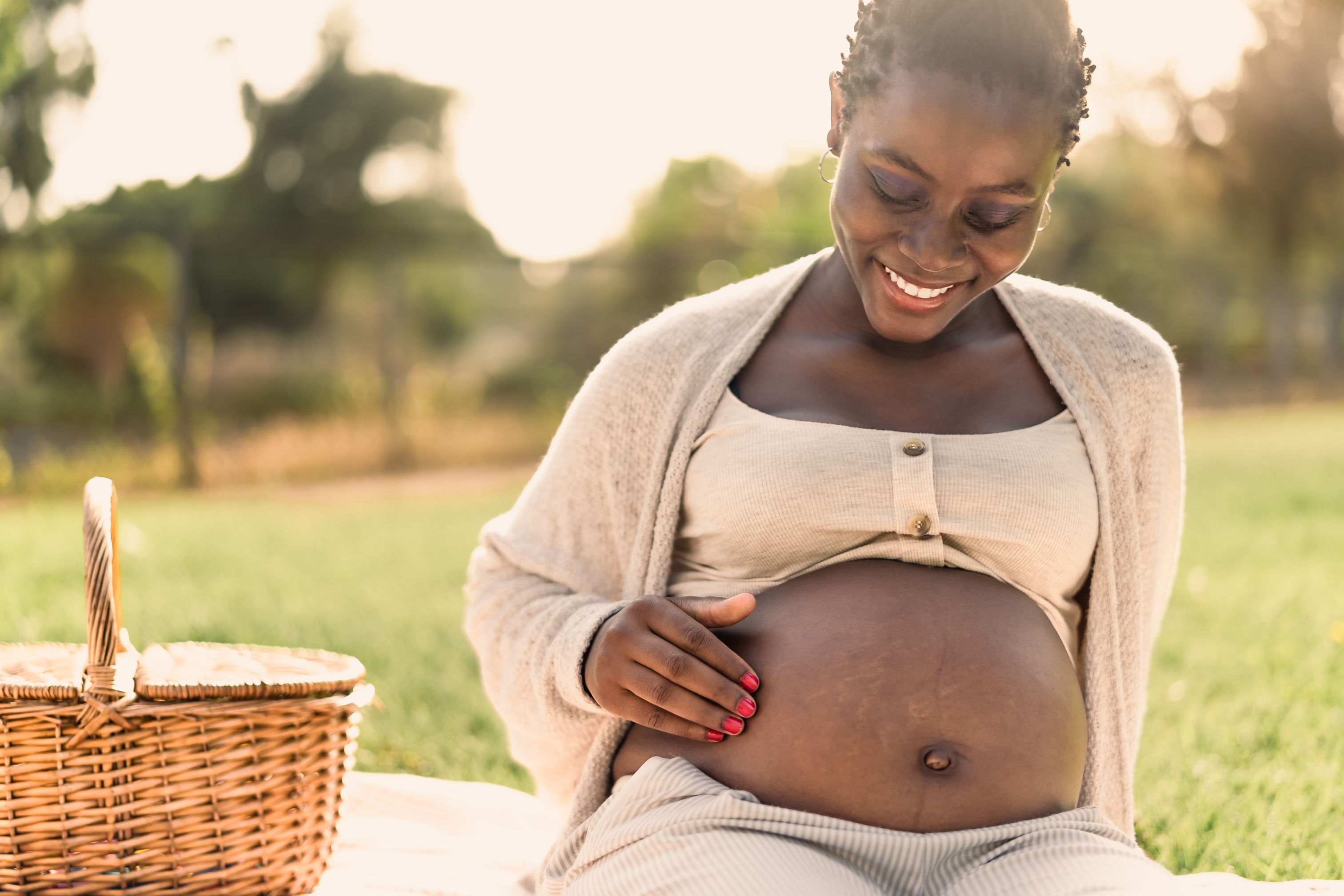 African,Woman,Caressing,Her,Pregnant,Belly,While,Doing,A,Picnic