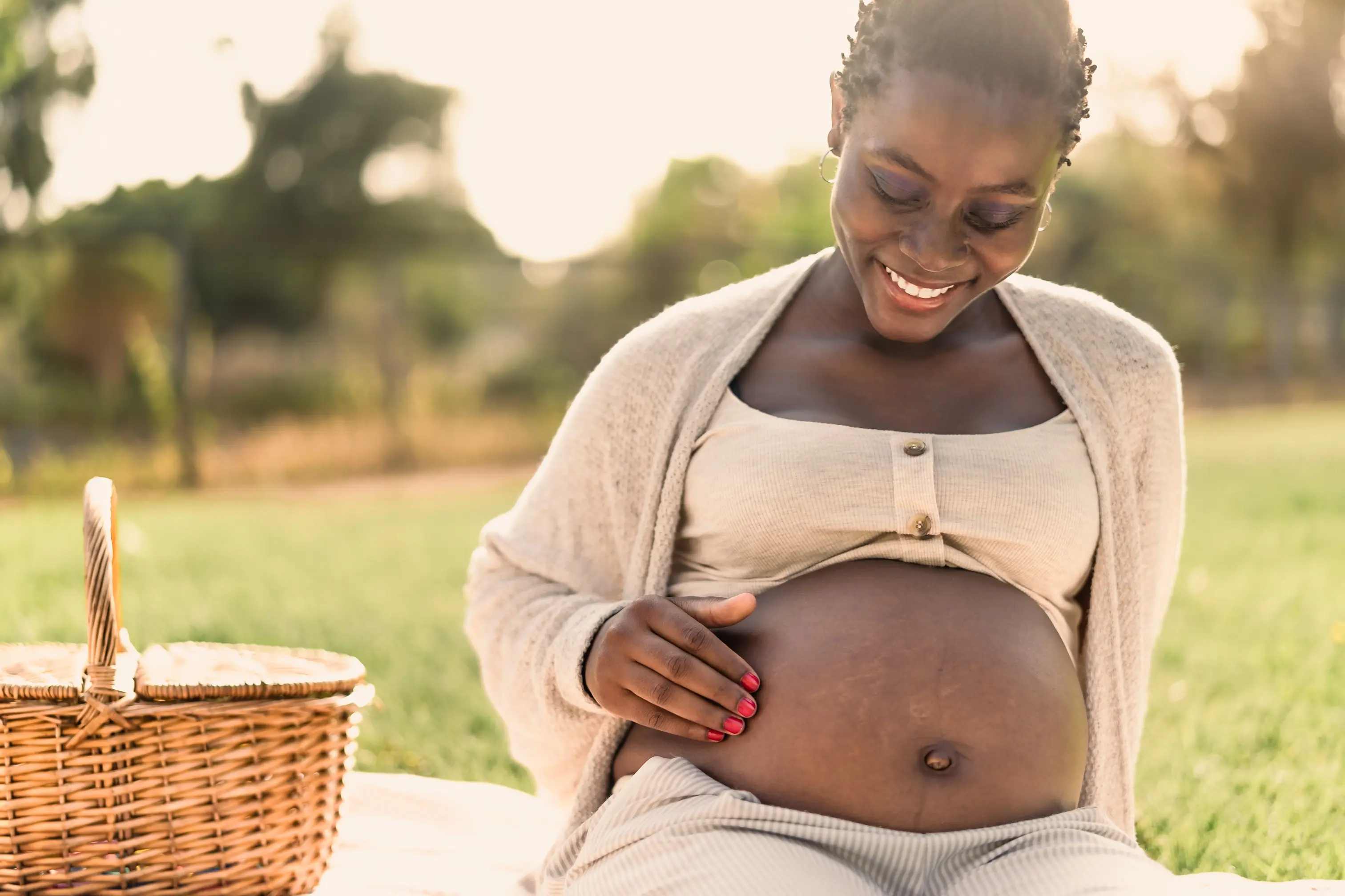 African,Woman,Caressing,Her,Pregnant,Belly,While,Doing,A,Picnic